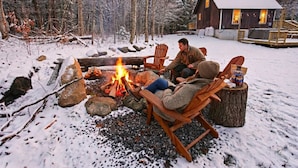 A cabin with a fire pit, wooden chairs, and a snow-covered landscape. - Dream Stratton Forest Cabin w/Hot Tub & Fast WiFi (Stratton)