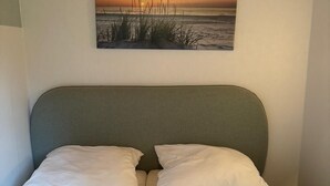A double bed with a grey headboard and white bedding, a painting of a sunset on the wall, and a wooden ceiling. - Cozy vacation bungalow with breathtaking lake view (Tignale)