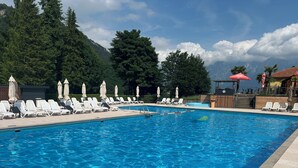 A swimming pool with lounge chairs and umbrellas, surrounded by trees and mountains. - Cozy vacation bungalow with breathtaking lake view (Tignale)