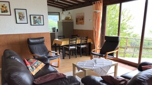 A living room with a sofa, two armchairs, a dining table with chairs, a small table with a glass, and a view of greenery through large windows. - Cozy vacation bungalow with breathtaking lake view (Tignale)
