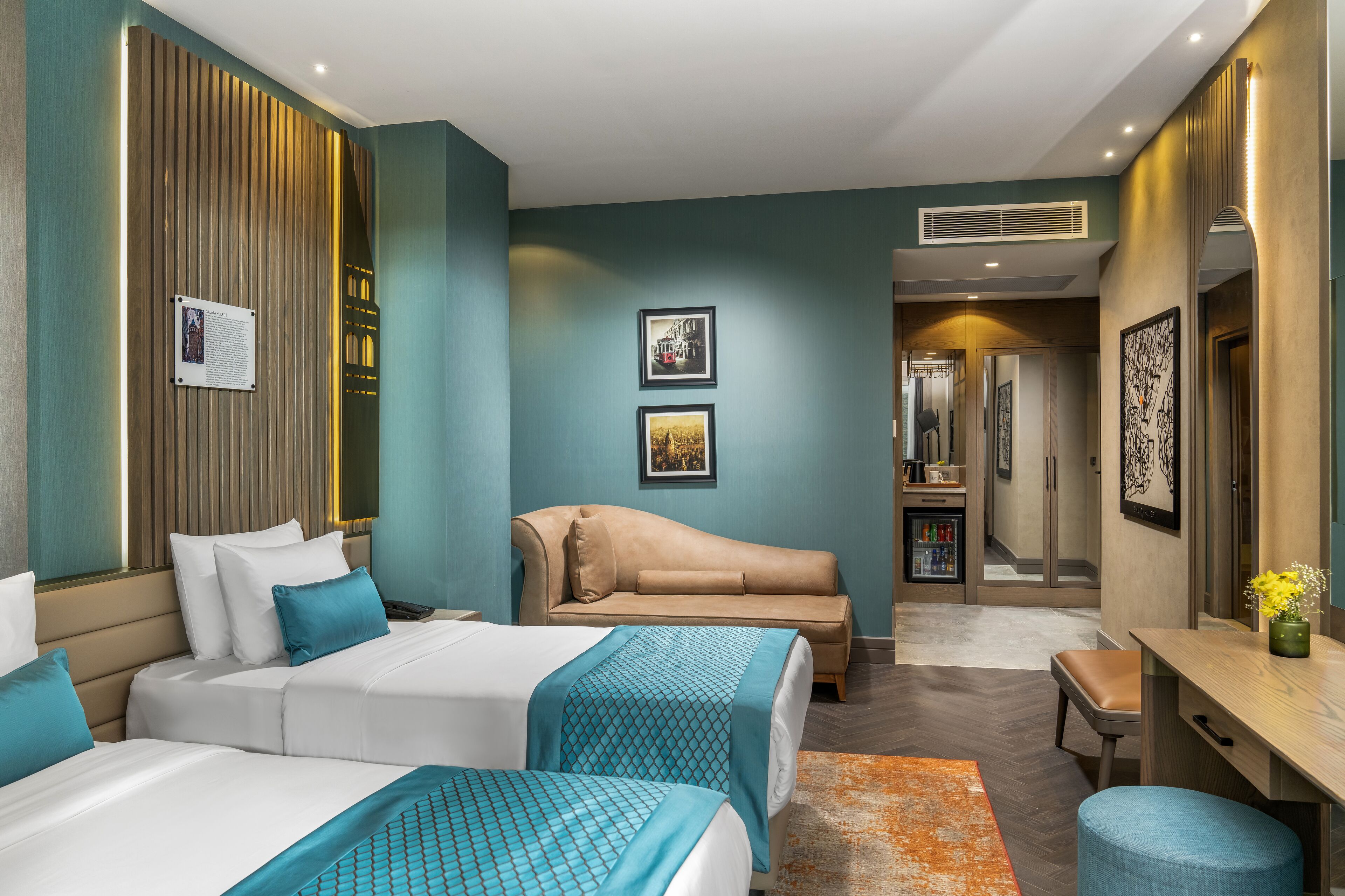 A hotel room with two beds, a sofa, a desk, and a bathroom visible in the background.