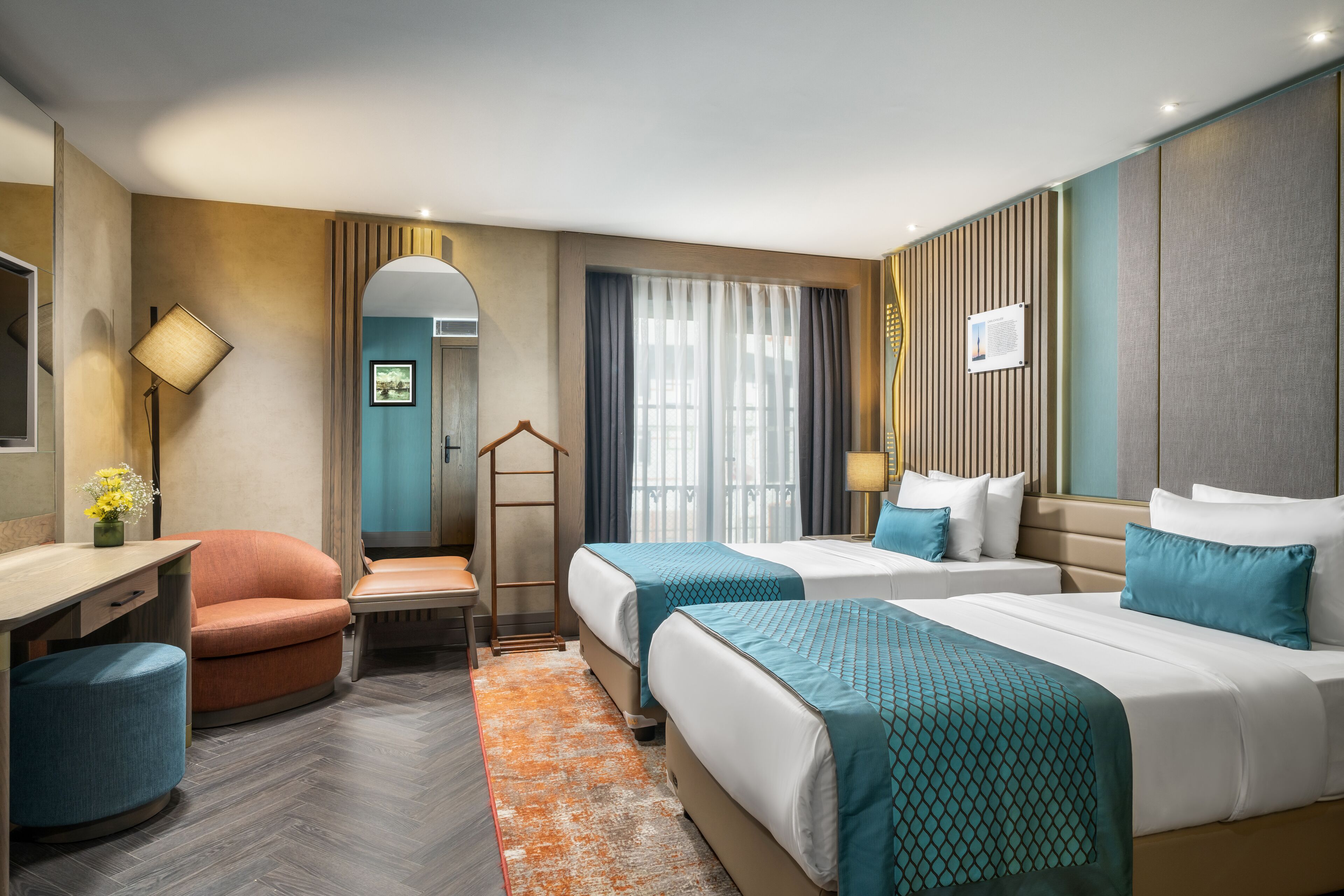 Quarto de hotel com duas camas, uma escrivaninha, uma cadeira e um guarda-roupa.