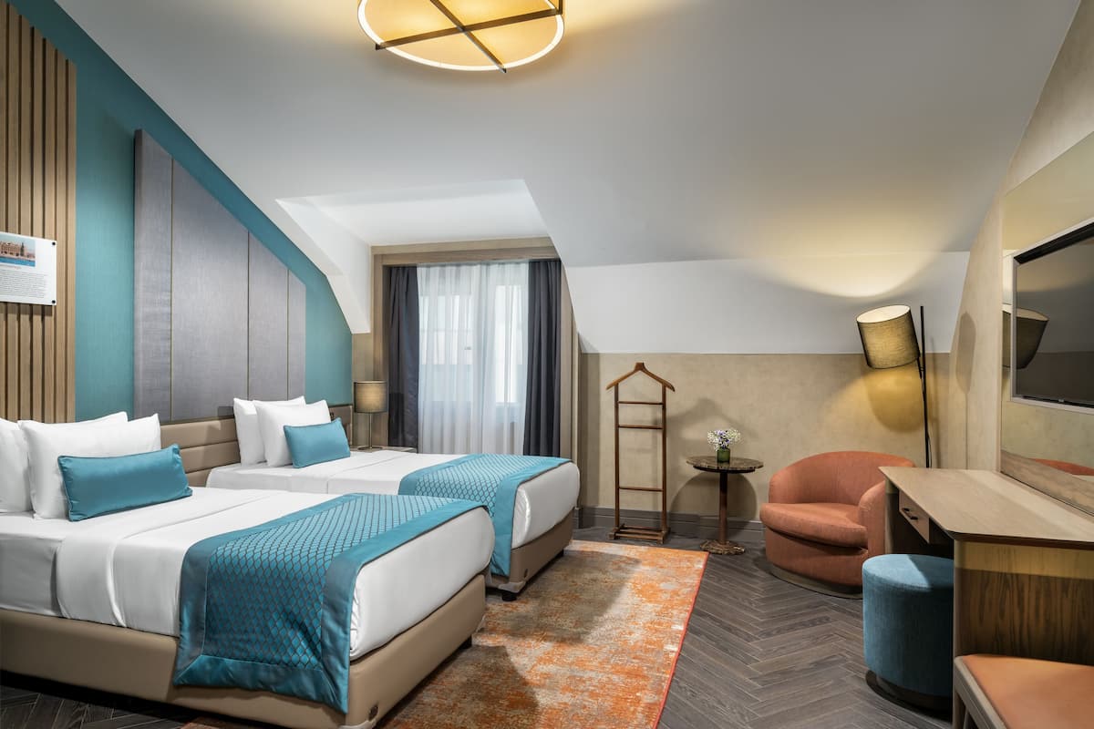 Une chambre d’hôtel avec deux lits, un bureau, une chaise, une télévision et une fenêtre avec des rideaux.
