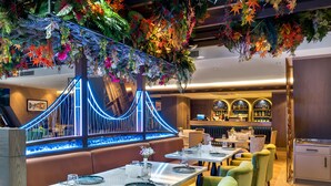 Un restaurant au décor moderne, avec une installation lumineuse originale en forme de pont, des aménagements de sièges et un espace bar.