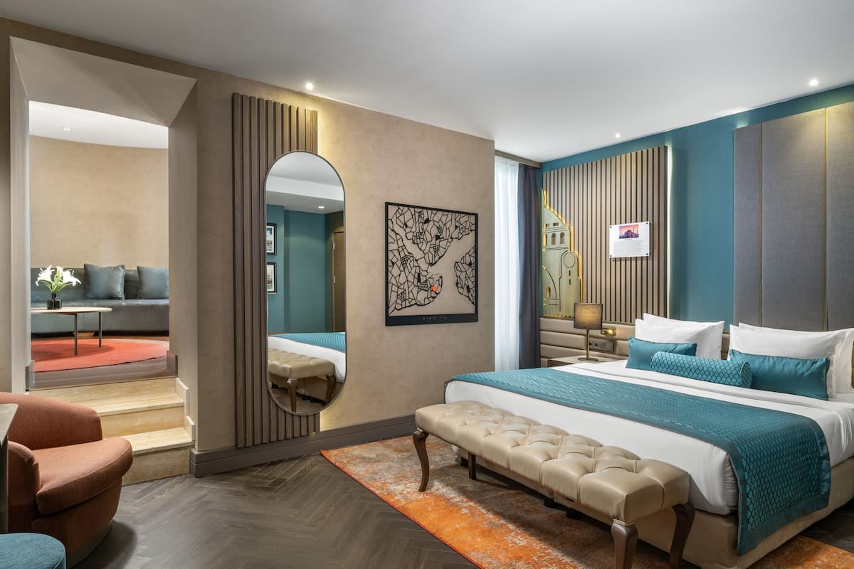 Une chambre d’hôtel moderne dotée d’un grand lit, d’un coin salon avec un canapé et un fauteuil, d’une petite table et d’un miroir.