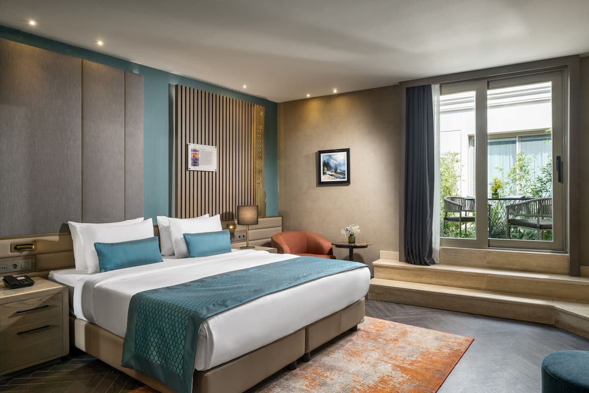 Une chambre d’hôtel moderne, dotée d’un grand lit, d’un bureau, d’une chaise et d’une fenêtre donnant sur un paysage verdoyant.