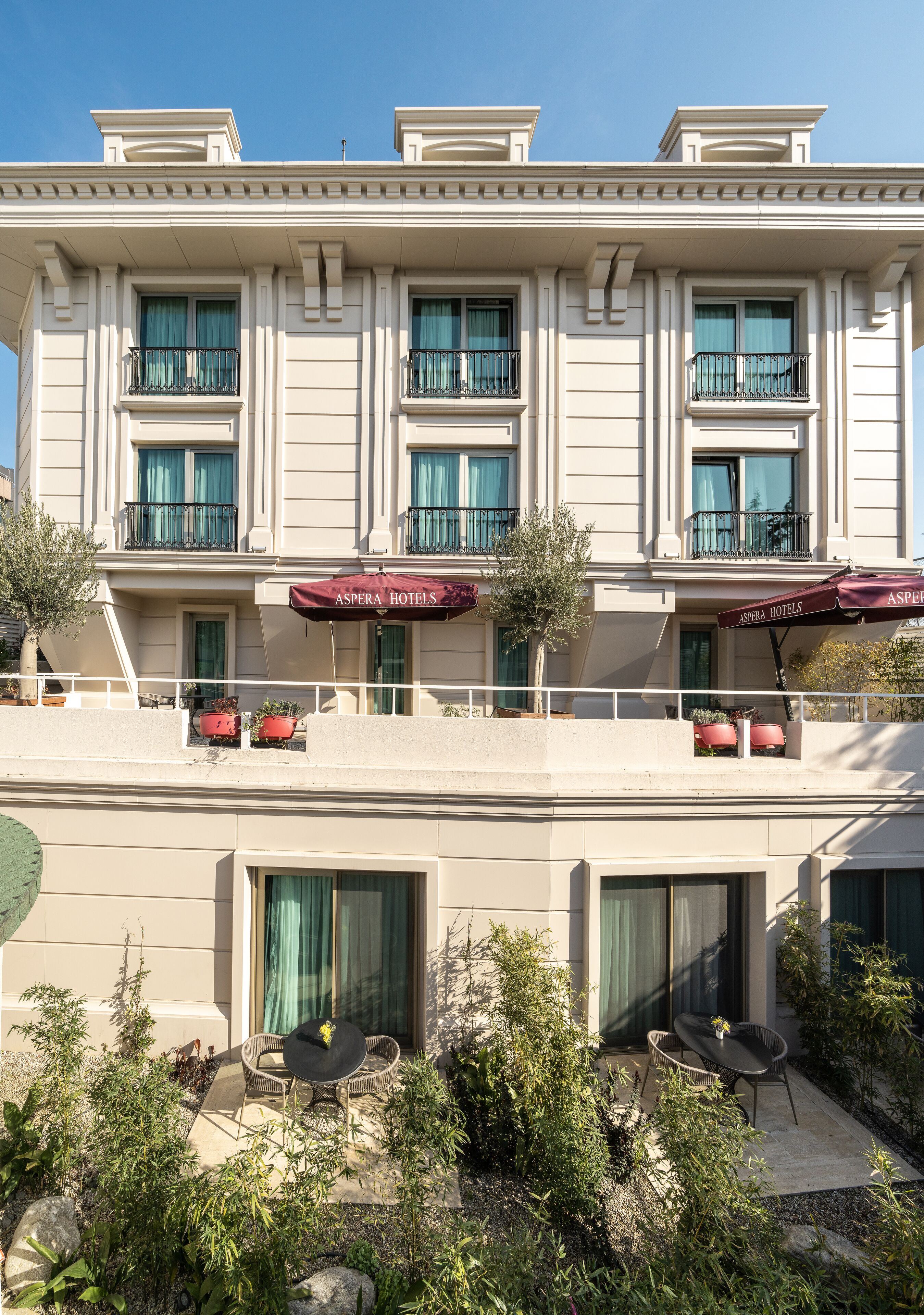 A hotel with a symmetrical facade, large windows, and outdoor seating areas with umbrellas.