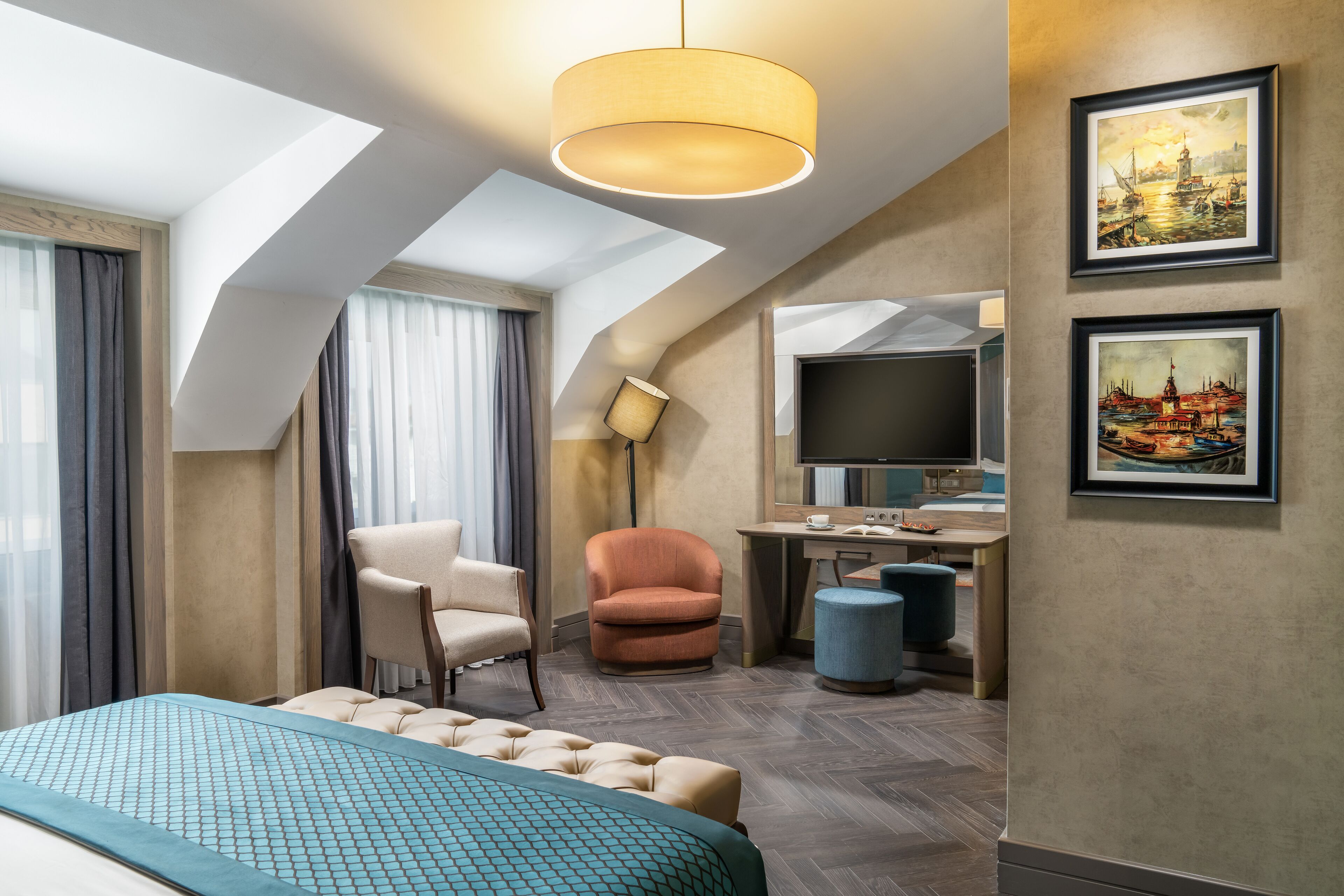 A modern hotel room with a large bed, a desk, a chair, a sofa, and a TV.
