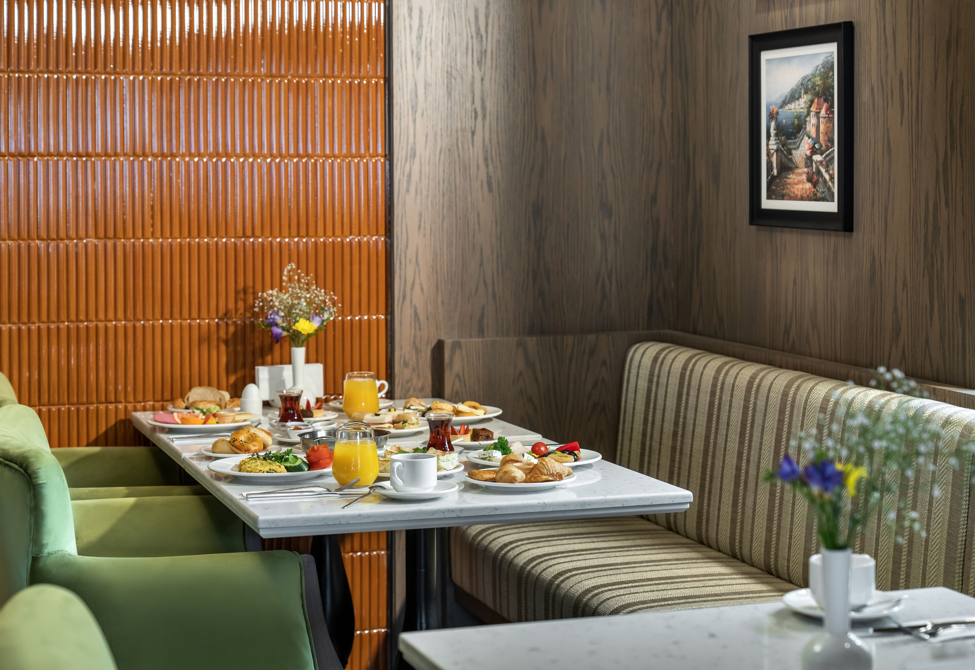 A breakfast setting with a table set for two, a bench, and a framed picture on the wall.