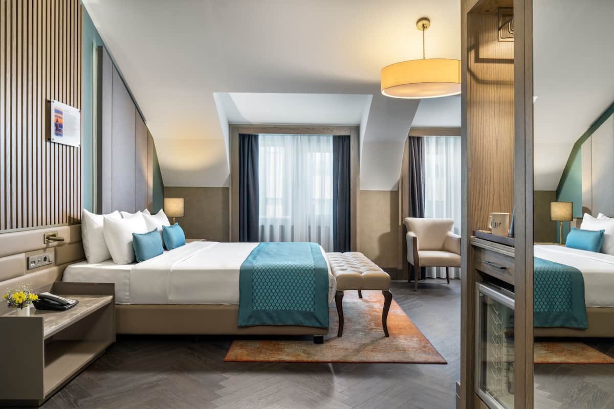 Une chambre d’hôtel moderne dotée d’un grand lit, d’un bureau, d’une chaise et d’une salle de bain fermée par des parois de verre.