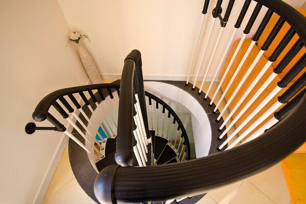 A spiral staircase with black and white railings, a handrail, and a carpeted floor.