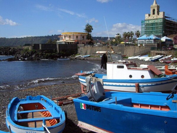 A coastal scene with boats docked along the shore, a building with a bell tower, and a clear sky.