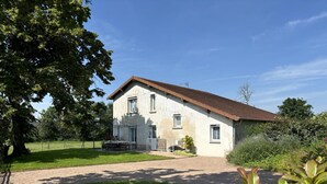 Une maison à deux étages, avec un toit en tuiles, une terrasse couverte et une pelouse bien entretenue.