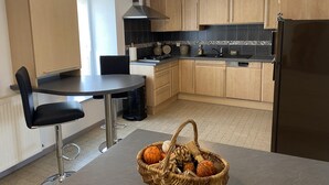 Une cuisine moderne avec des meubles en bois, une hotte de cuisine en acier inoxydable, un plan de travail noir et un coin repas comprenant une table ronde et des chaises noires.