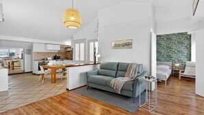 A modern living room with a sofa, a dining area with a table, and a kitchen in the background. - Rooftop - AC, Lake View With Terrace (Stresa)
