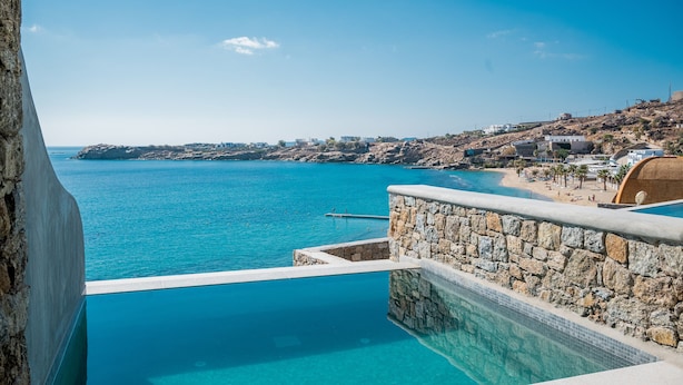 A stone pool with a view of the sea and a beach. - New Paradise Beach Resort- Adults Only (Mykonos)