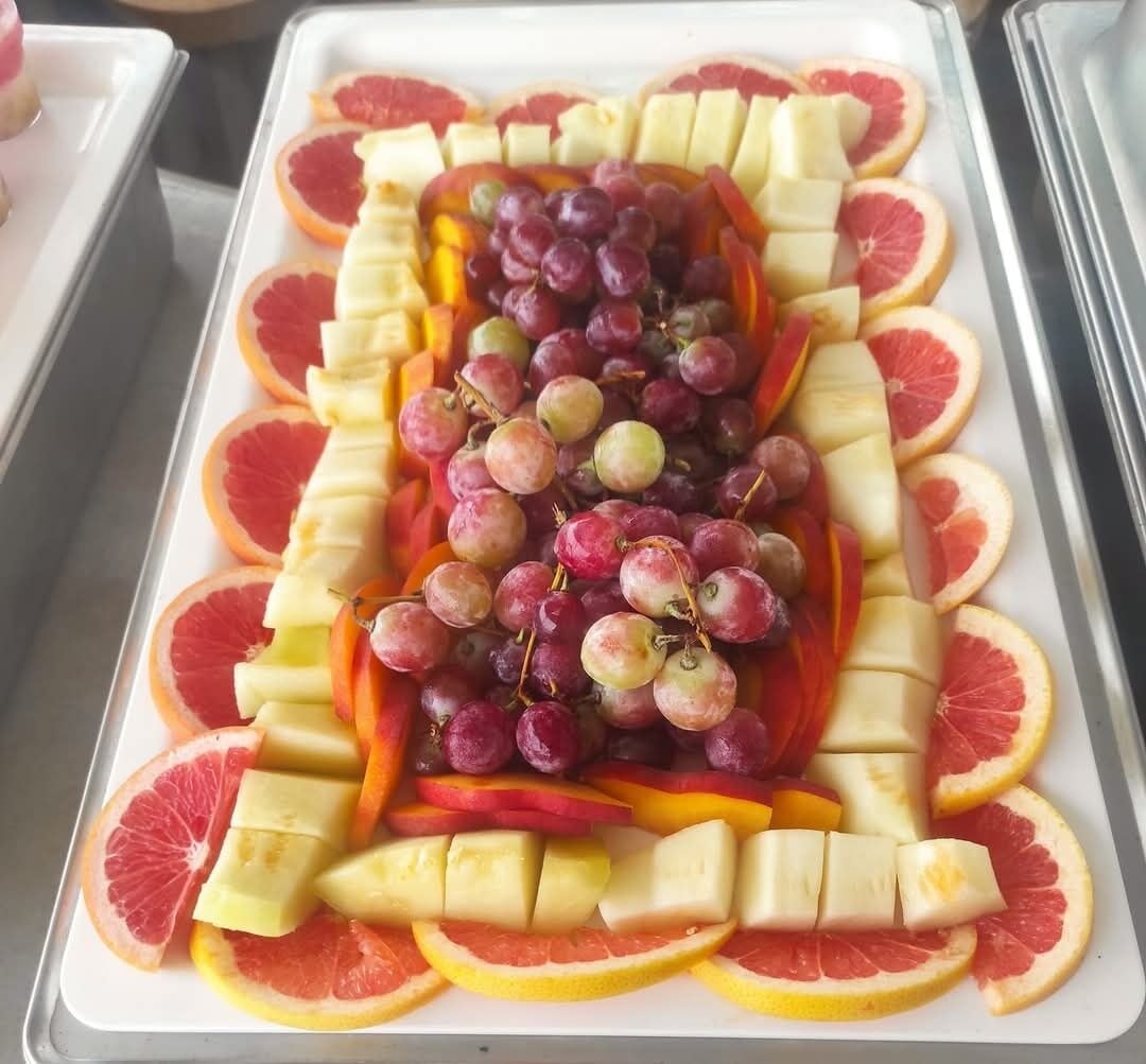 A tray of sliced fruits including grapefruit, apples, and grapes arranged in a decorative pattern.