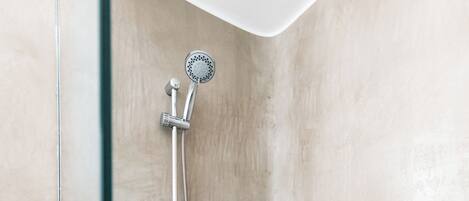 A corner shower with a glass door, a handheld showerhead, and a wall-mounted faucet.