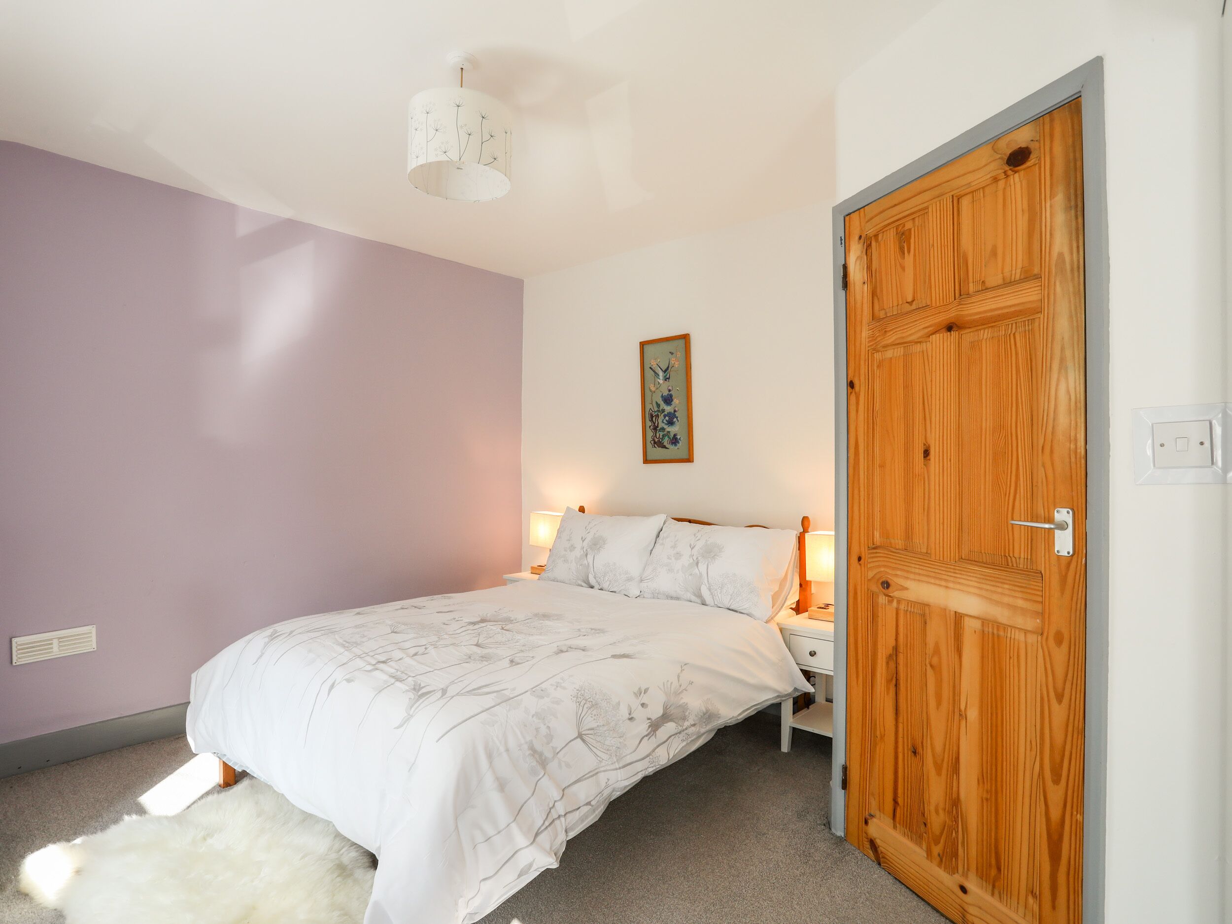 A bedroom with a bed, a nightstand, a wooden door, and a wall-mounted lamp.