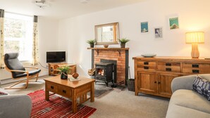 A cozy living room with a fireplace, a television, a sofa, and a wooden cabinet. - 9 Ty Du Road (Caernarfon)