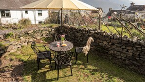 A round table with chairs and a table umbrella in a garden with a stone wall and a mountain in the background. - 9 Ty Du Road (Caernarfon)