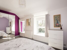 Quarto com cama grande, cômoda, espelho e janela com cortinas.