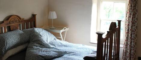 A bedroom with a bed, a desk, and a window with curtains.