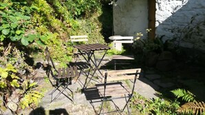 Un espace extérieur aménagé avec une table et des bancs, entouré de verdure et bordé d’un bâtiment en pierre.