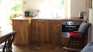 Une cuisine compacte dotée de meubles en bois, d’un four encastré, d’un évier et d’une fenêtre laissant entrer la lumière naturelle.