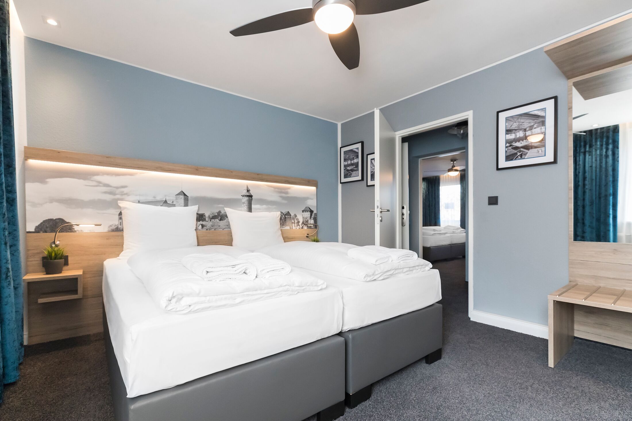 A modern hotel room with a large bed, a ceiling fan, and a view of the city through the window.