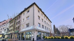 Un edificio de varios pisos con un bar-cafetería y letrero de hotel, mesas al aire libre y cielo despejado.