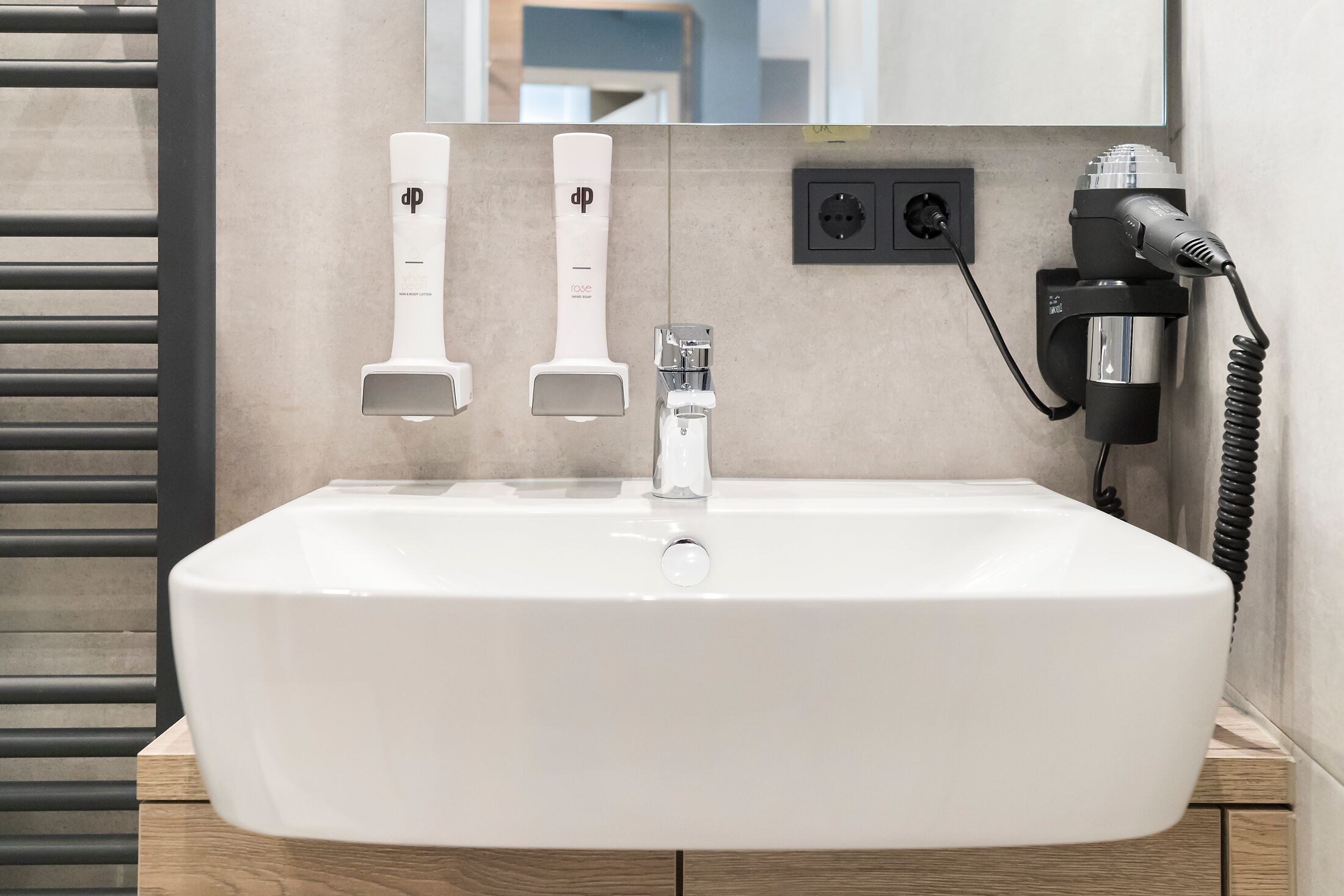 Un baño con lavamanos blanco, dos porta cepillos de dientes, un secador de pelo y un espejo.
