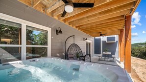 Una vasca idromassaggio in un'area esterna coperta, con tetto in legno, zona relax con tavolo e sedie, e vista sul paesaggio circostante.