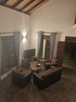 Ein Wohnzimmer mit Fernseher, Couchtisch, gemusterten Sofas und einer Schiebetür aus Glas.