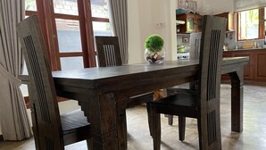 Un coin repas avec une table et des chaises en bois, un vase avec une plante, et une cuisine en arrière-plan.