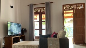 Une chambre avec un lit, un téléviseur posé sur un meuble en bois, une porte agrémentée d’un paravent décoratif et une vue sur l’extérieur.