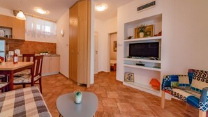 Ett kompakt bostadsutrymme med en matplats, ett litet kök och en tv som står på en hylla.