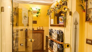 A hotel room with a glass shower enclosure, a wooden cabinet with toiletries, and a mirror with a decorative sunflower arrangement. - Alloggio dei Vassalli, In the Heart of the Historic Center (Naples)
