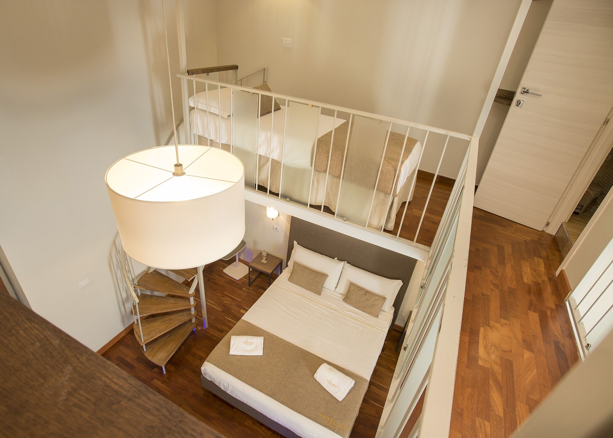 A bedroom with a bed, a nightstand, a lamp, and a staircase leading to an upper level.