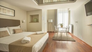A hotel room with a large bed, a small table with chairs, a potted plant, and a view of the outdoors through a window. - Palazzo Depretis Naples (Naples)
