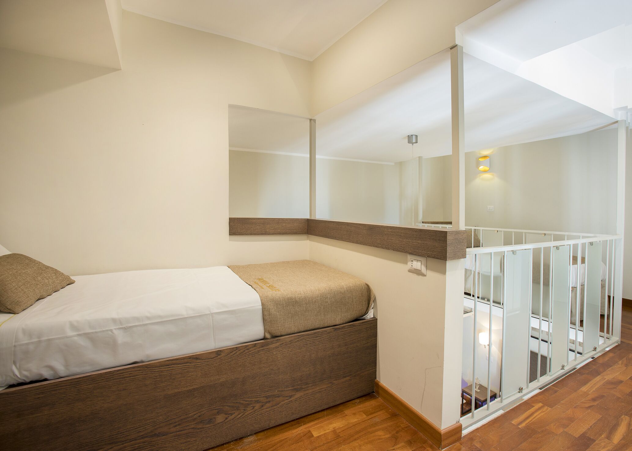 A bedroom with a bed, a wooden bench, a white railing, and a mirror on the wall.