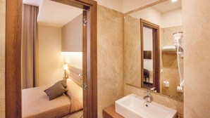 Une chambre d’hôtel comprenant un lit, une salle de bain avec un lavabo et un miroir, et un sèche-cheveux.