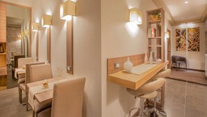 Un espace repas moderne avec de hautes tables et des tabourets de bar, un comptoir en bois agrémenté d’un vase, et une bibliothèque contenant des livres et une plante.