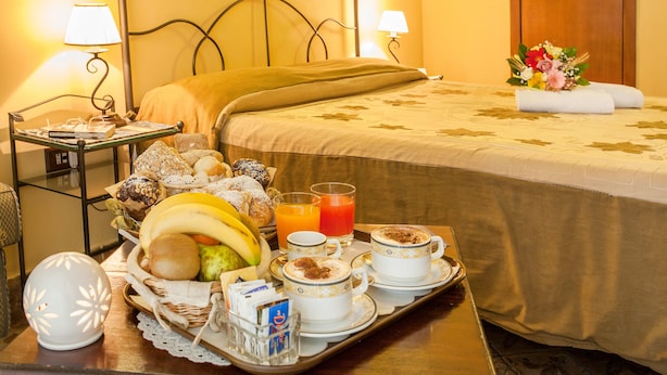 A hotel room with a neatly made bed, a tray with breakfast items, and a bouquet of flowers on the bed. - Double Triple Room in Naples City Center (Naples)