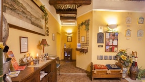 A cozy hotel lobby with a wooden reception desk, a bed, and a wall decorated with clocks and framed pictures. - Double Triple Room in Naples City Center (Naples)