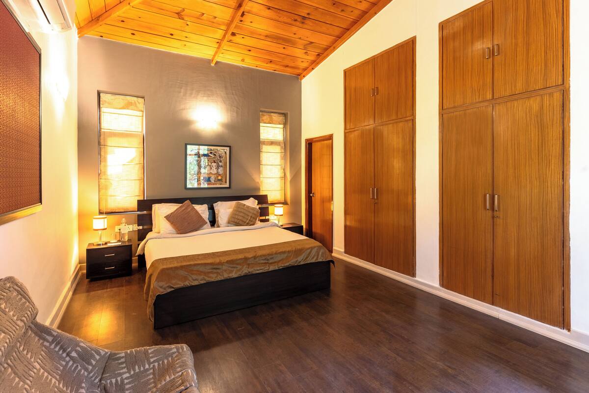 A bedroom with a large bed, wooden wardrobe, and a nightstand with a lamp.