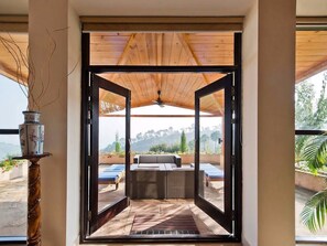 Uma área de pátio aberta com teto de madeira, um sofá e vista para uma piscina e vegetação.
