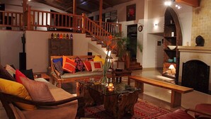 A cozy living room with a wooden staircase, a sofa with colorful cushions, a glass coffee table, and a fireplace. - Tree of Life Junoon in the Hills, Kainchi Dham (Kosiyakutoli)