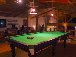 Una mesa de billar con bolas, una silla y un sofá en una habitación con vigas de madera y luces colgantes.
