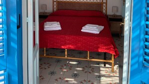 A bedroom with a red bedspread, a wooden headboard, and a floral-patterned floor. - House "sole" - Unique Panorama (Lipari)